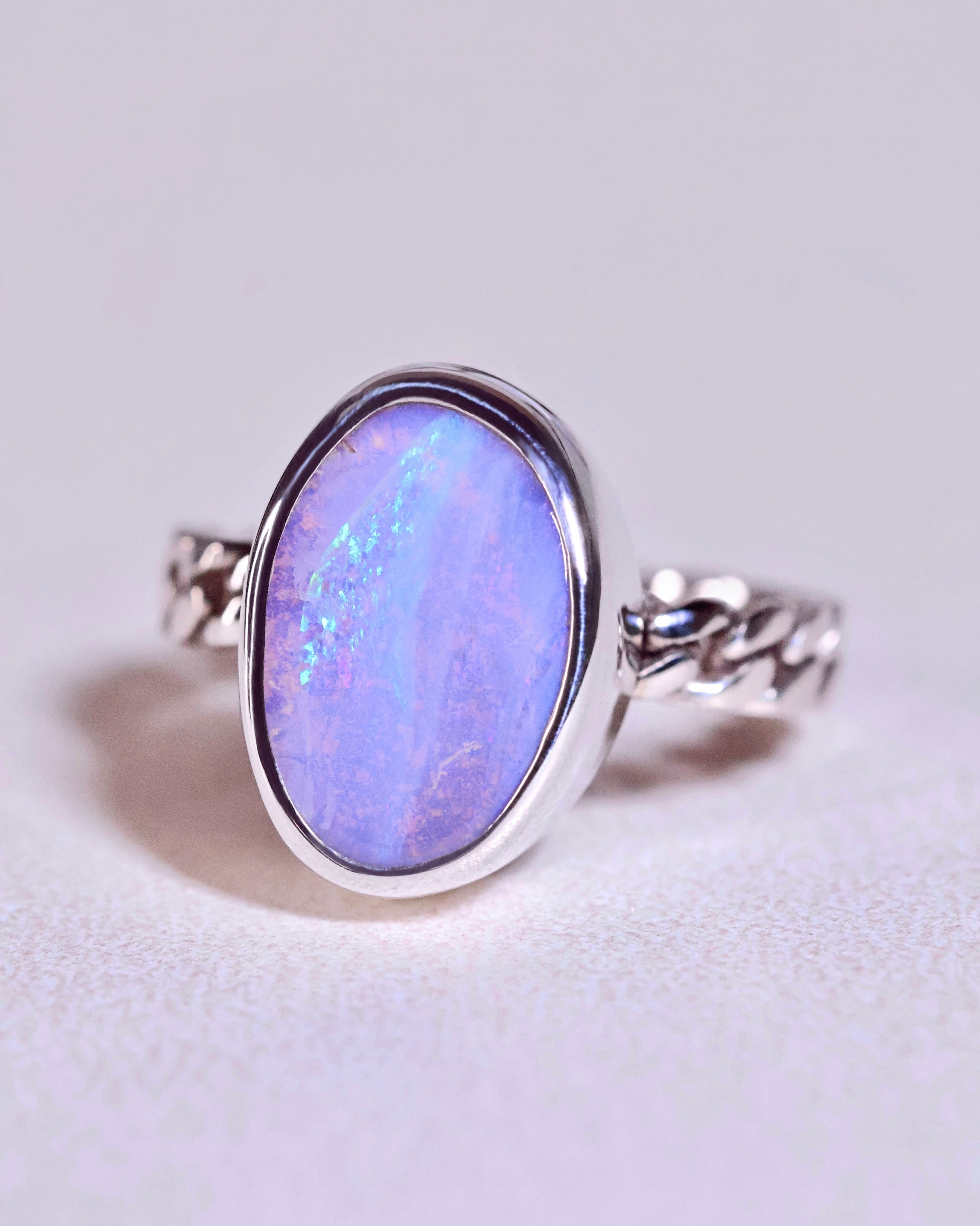 The Boulder Opal Ring by Lilac Sky Studio features a large oval blue opal set in a twisted sterling silver band, photographed on a light background—an elegant piece of jewelry.