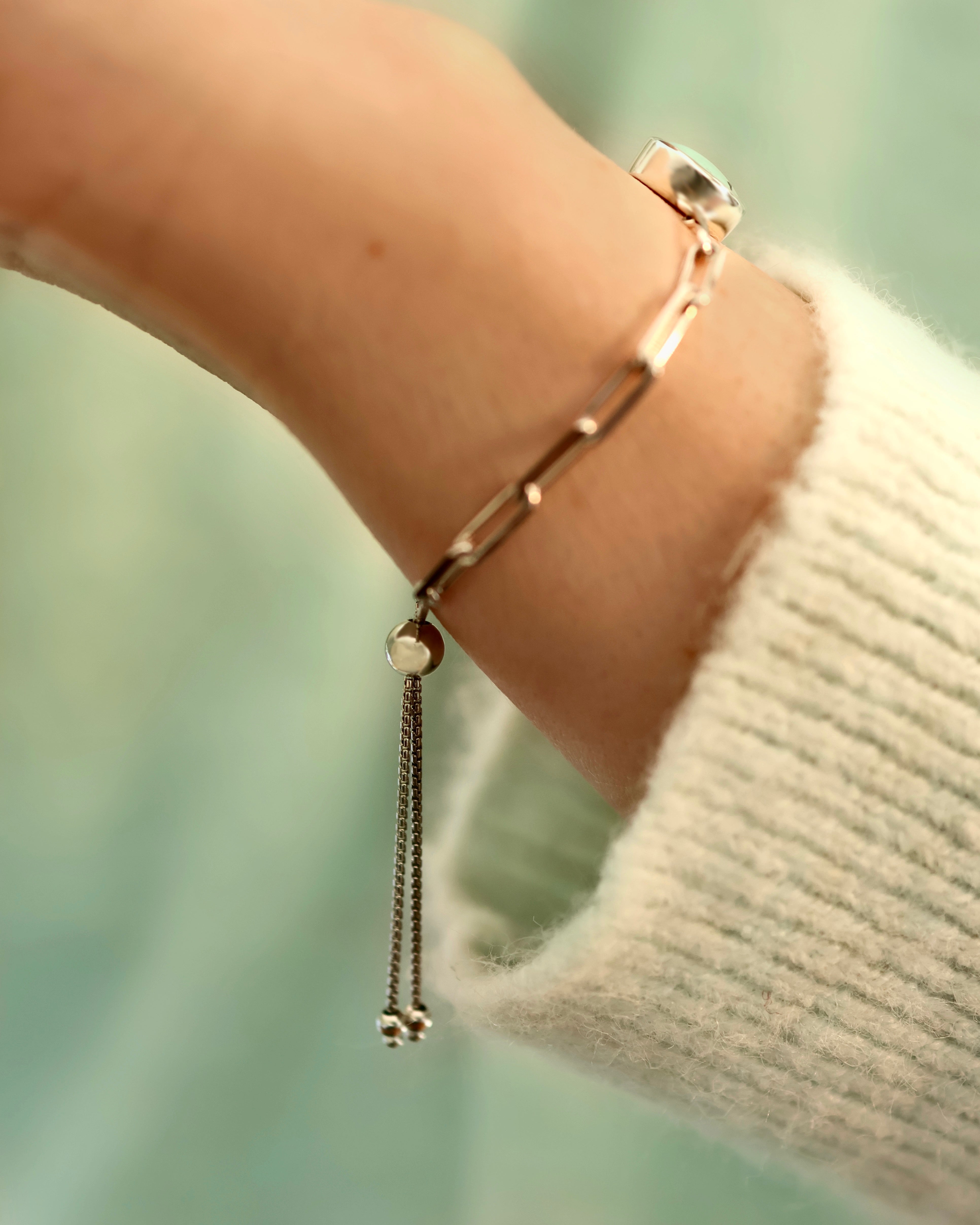 A close-up of a wrist wearing Lilac Sky Studio’s Treasure Mountain Turquoise Bracelet No. 2, featuring a turquoise charm and adjustable gold cable chain, styled with a light knit sweater against a softly blurred background.