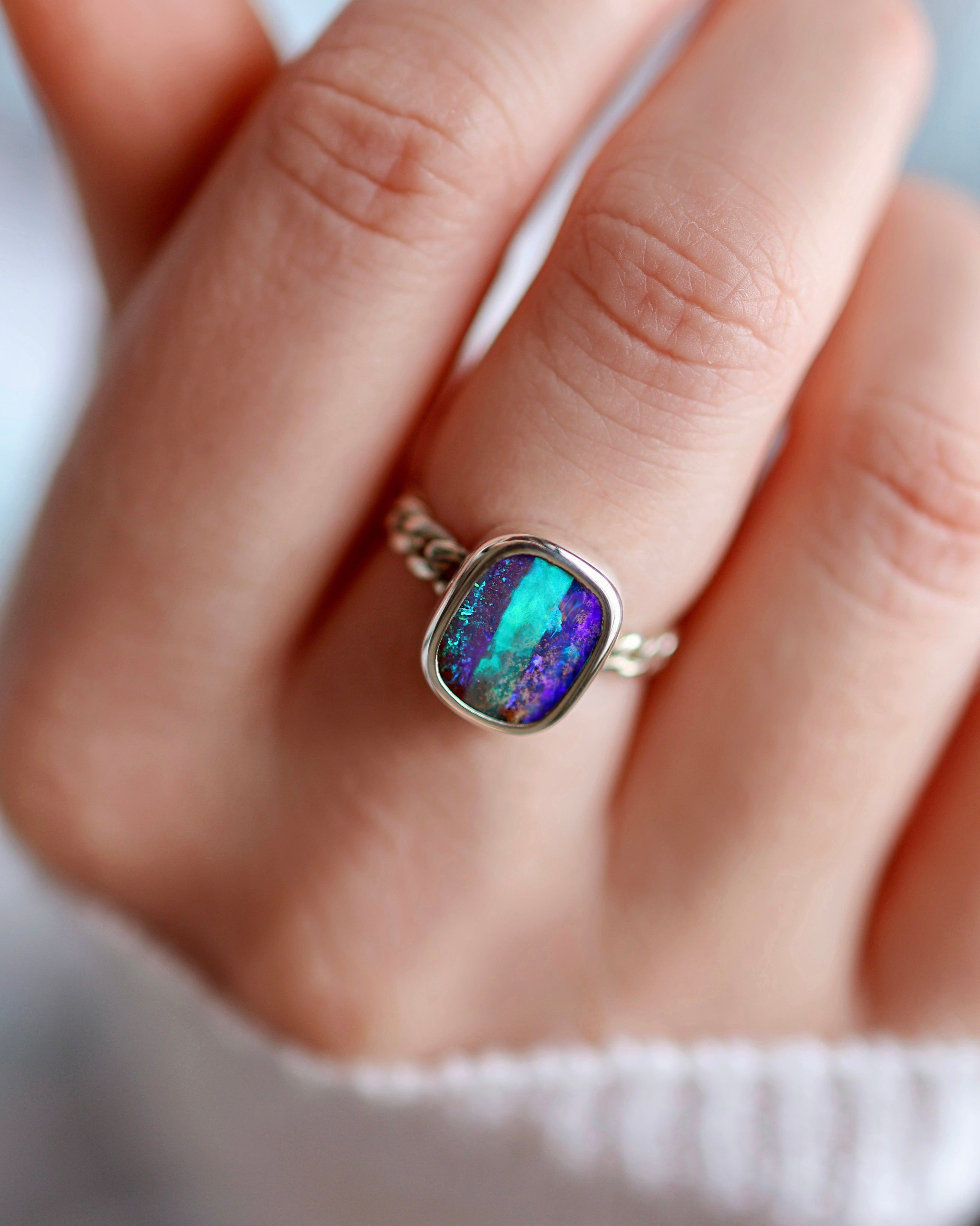 A hand wears the Lilac Sky Studio Pipe Opal Ring, a sterling silver piece featuring a rectangular natural opal with vivid blue, green, and purple colors.