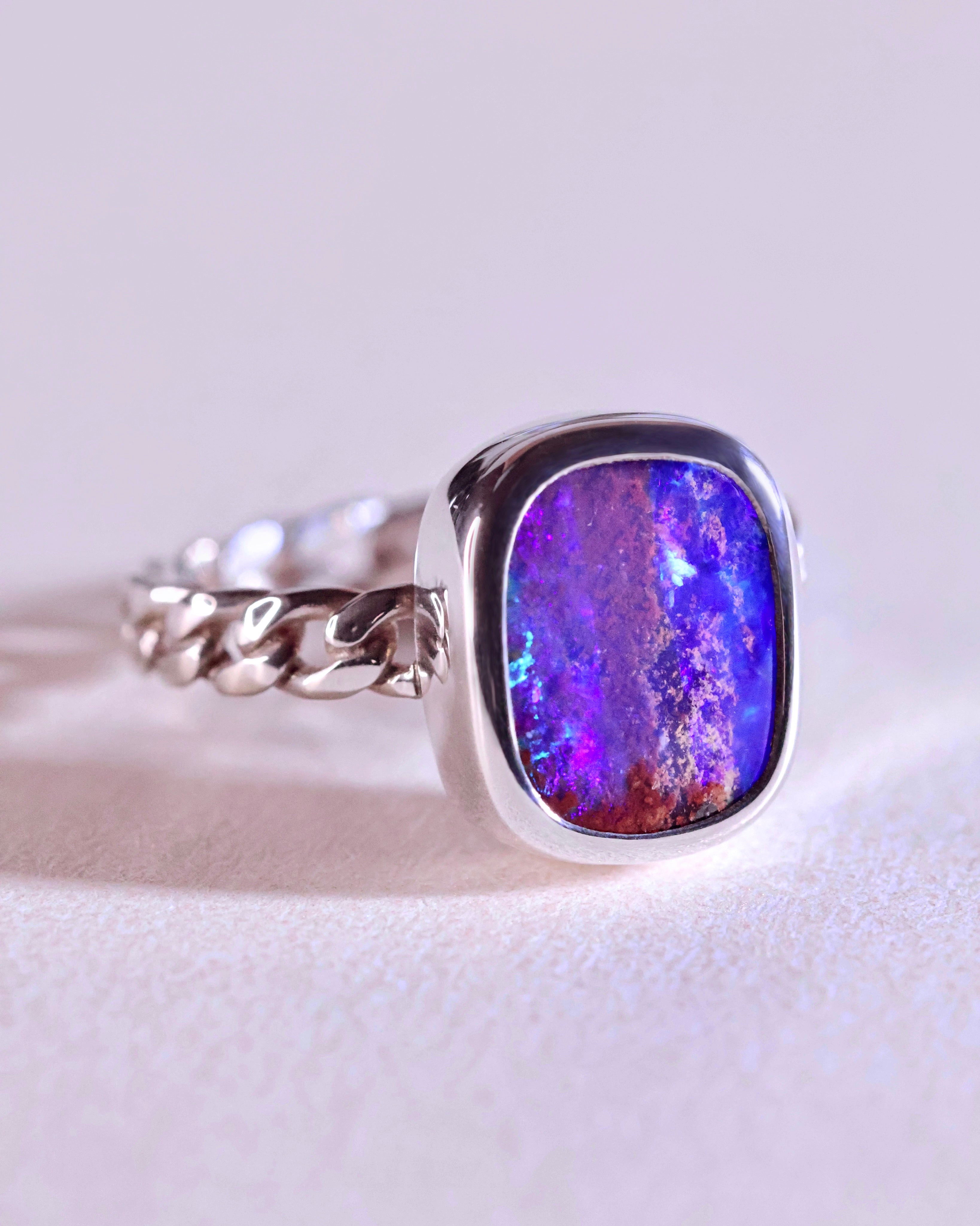 The Pipe Opal Ring by Lilac Sky Studio features a thick silver chain-link band and a square natural opal gemstone, shown resting on a light surface.
