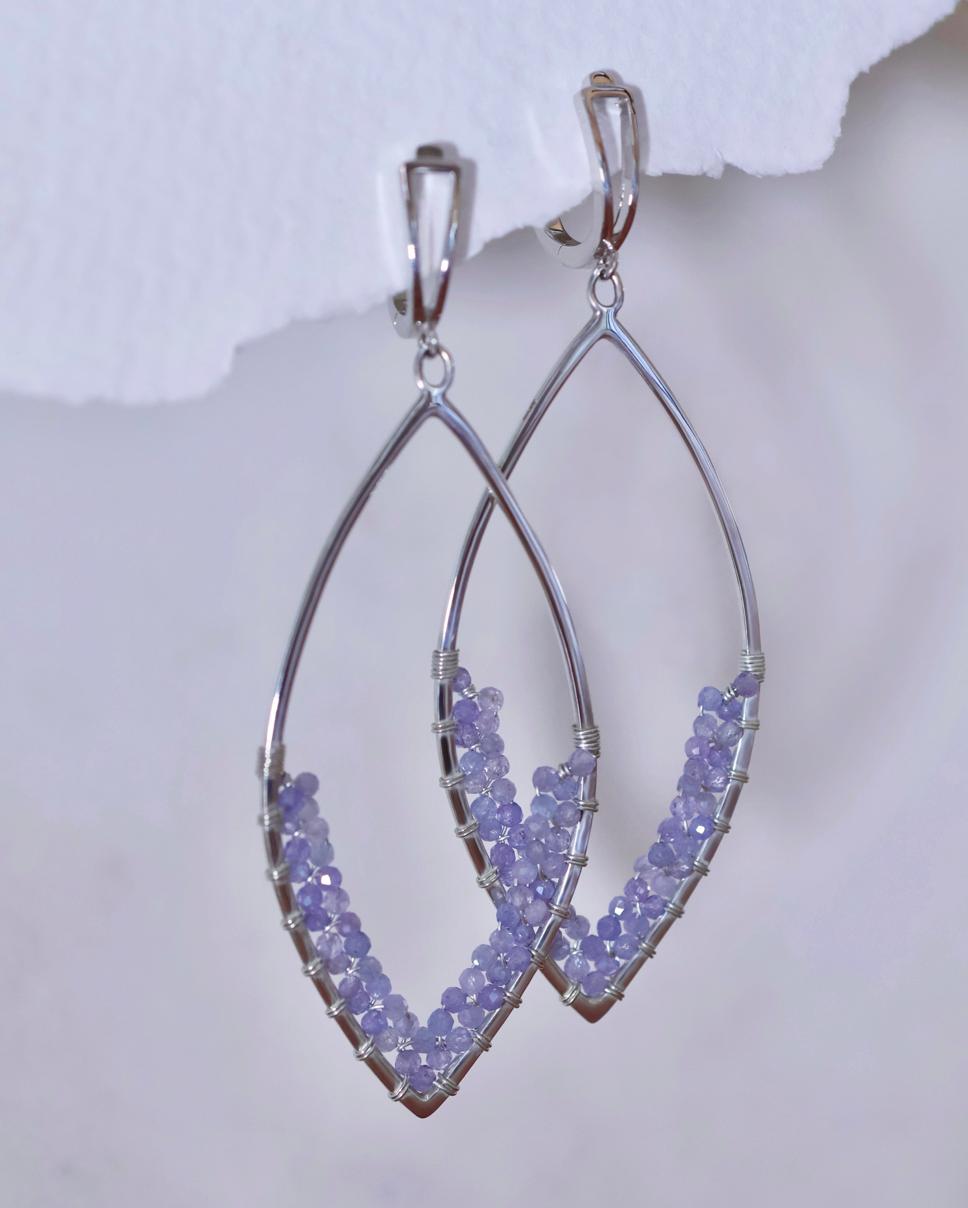 The Tanzanite Earrings by Lilac Sky Studio feature sterling silver dangle frames in a marquise shape, each adorned with handwoven Tanzanite beads beautifully arranged along the lower curve.