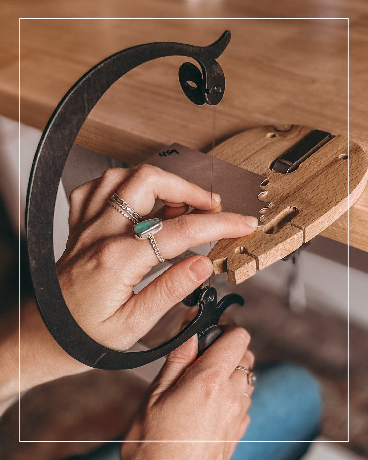 Close-up of hands using a jeweler’s saw to cut a piece of wood held in a wooden clamp on a workbench, preparing the base for a handcrafted jewelry or gold inlay.