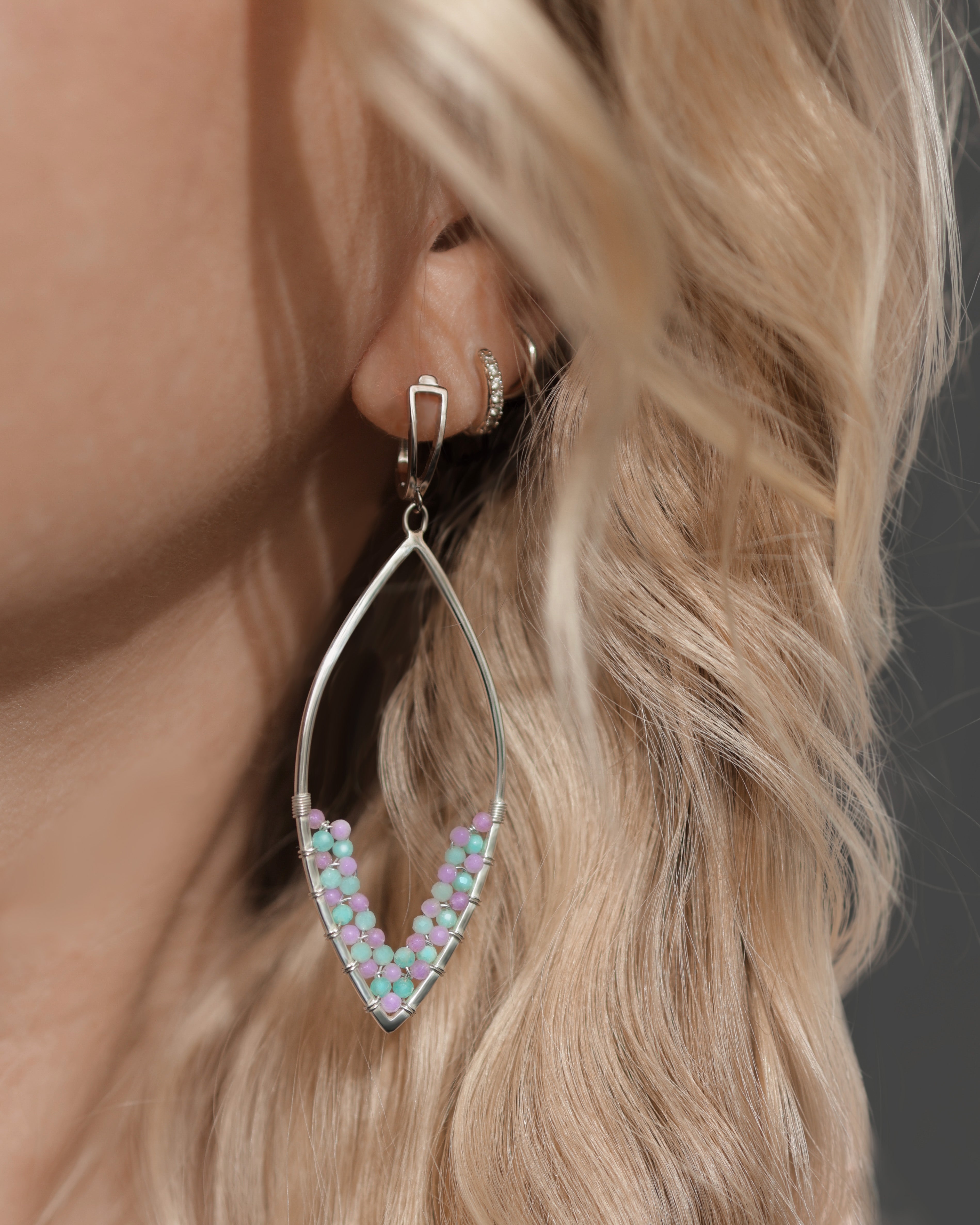 Close-up of a woman's ear with long, wavy blonde hair, wearing Lilac Sky Studio Amethyst + Amazonite marquise-shaped earrings with secure lever-back ear wires.