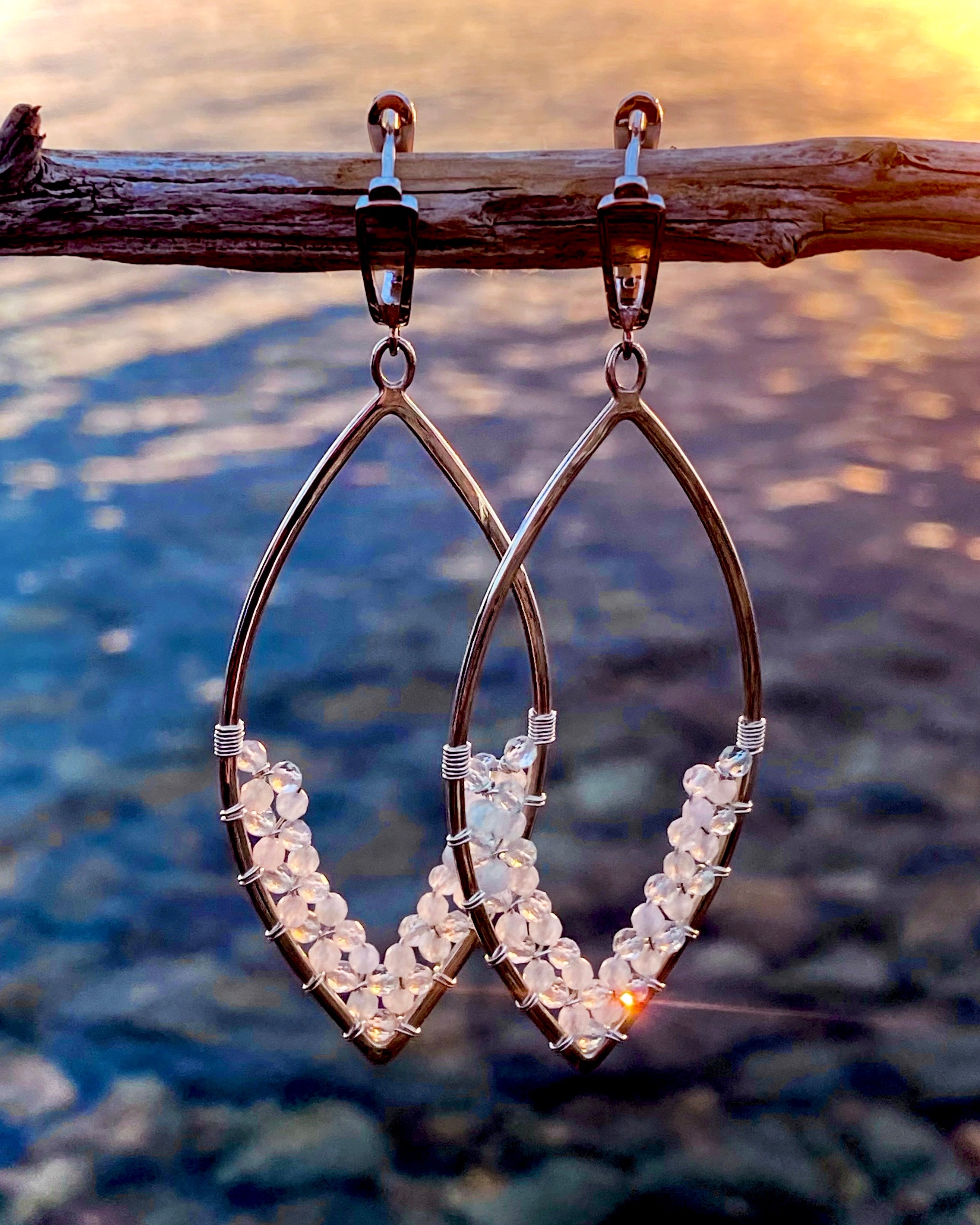 Aquamarine Earrings by Lilac Sky Studio: Sterling silver wire earrings with small clear beads and lever-back ear wires, shown hanging from a branch with sunlight on water in the background.