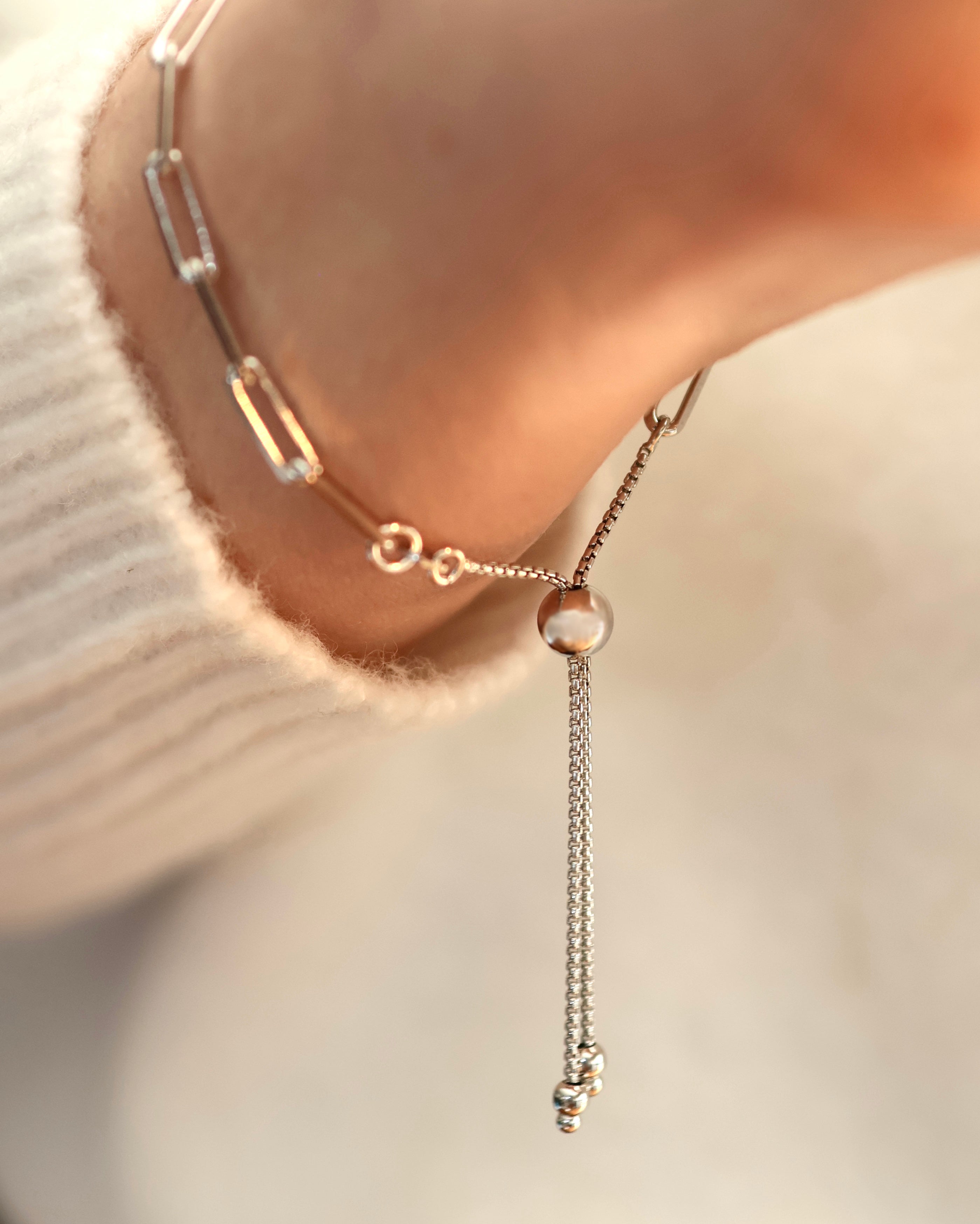 A close-up of the Lilac Sky Studio Treasure Mountain Turquoise Bracelet No. 1, featuring a turquoise bead and adjustable cable chain worn on a wrist, with part of a white sweater visible.