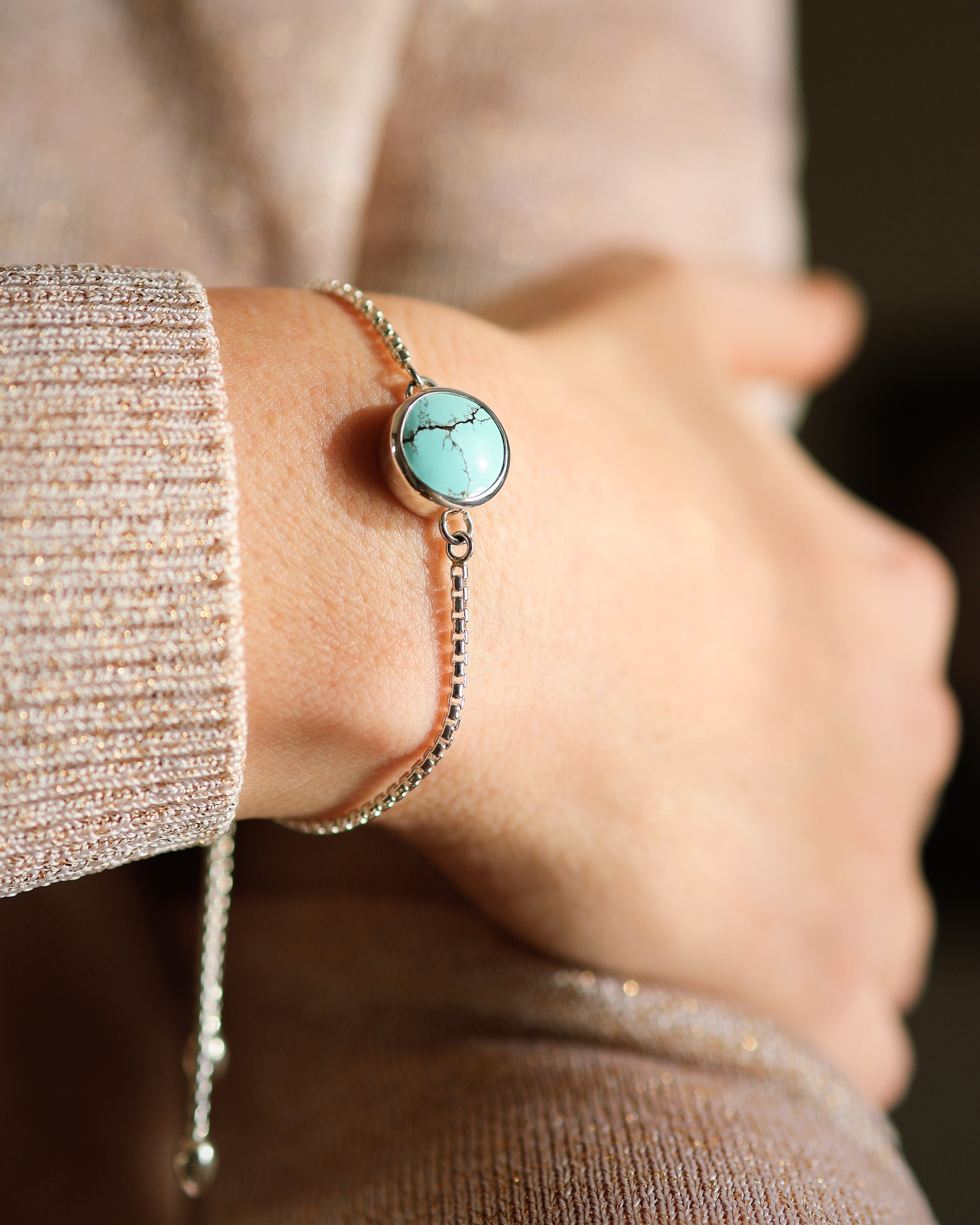 A close-up of a wrist wearing Lilac Sky Studio’s Cloud Mountain Turquoise Bracelet No. 4 in .925 sterling silver, featuring a round turquoise stone and adjustable box chain, shown against a beige shimmery sweater.