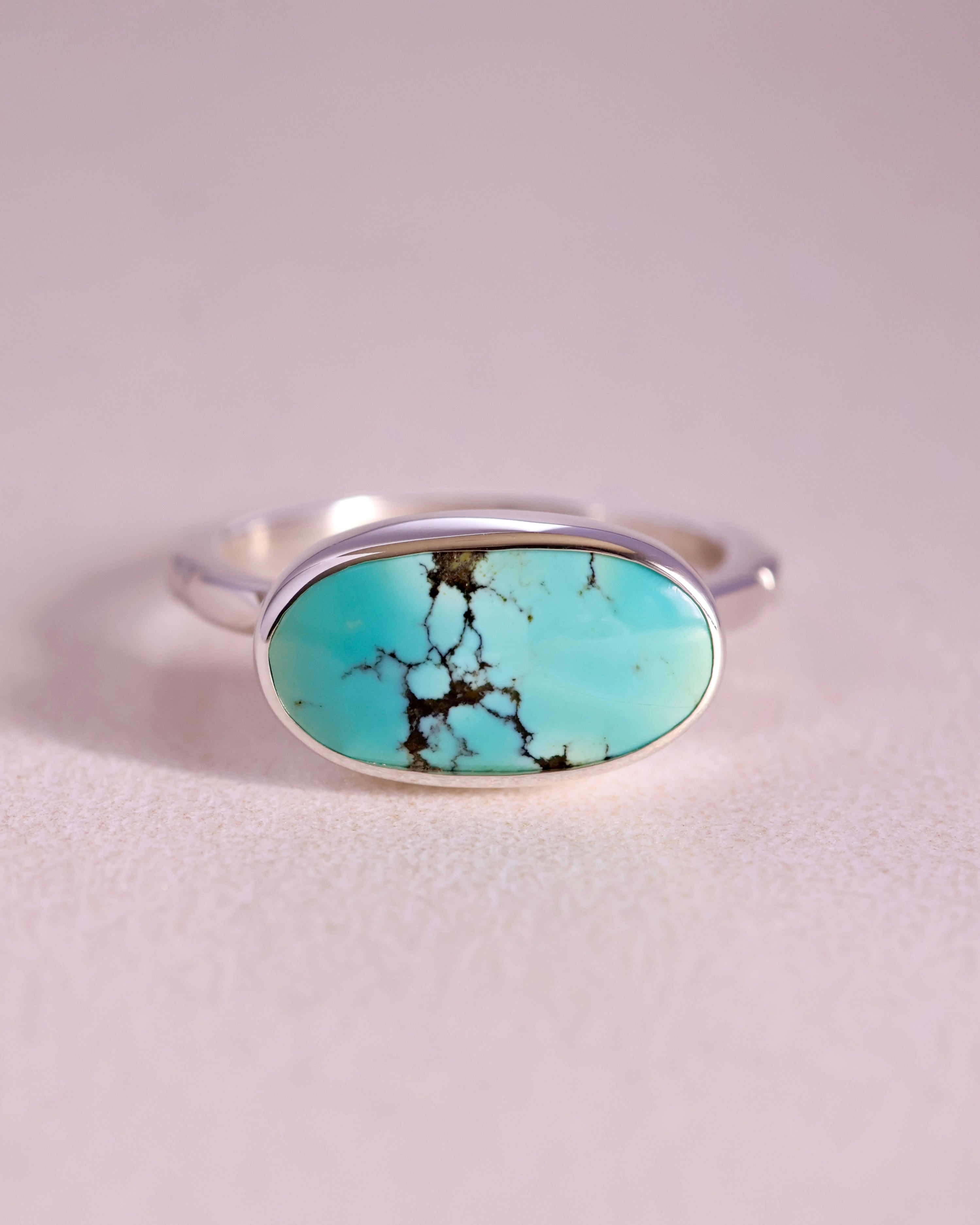 Turquoise stone ring with sterling silver faceted band on a light gray background