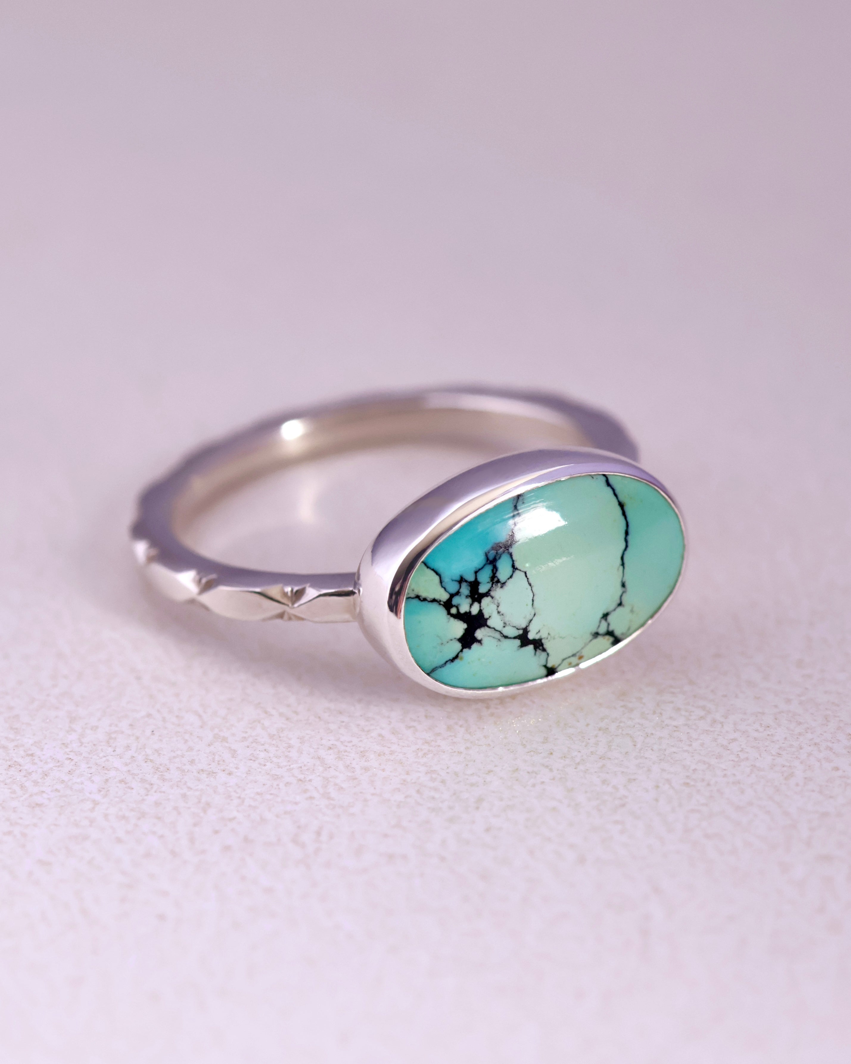 Sterling Silver ring with a turquoise stone and a starburst pattern band on a light gray background