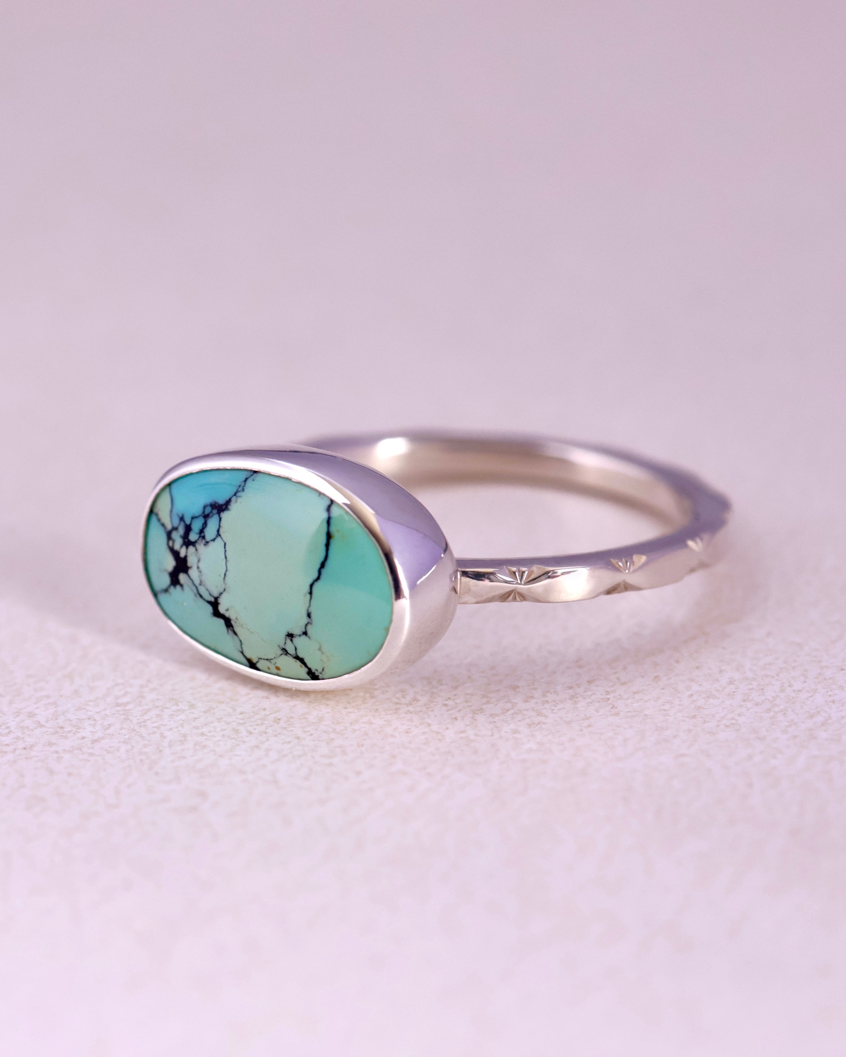 Sterling Silver ring with a turquoise stone and a starburst pattern band on a light gray background