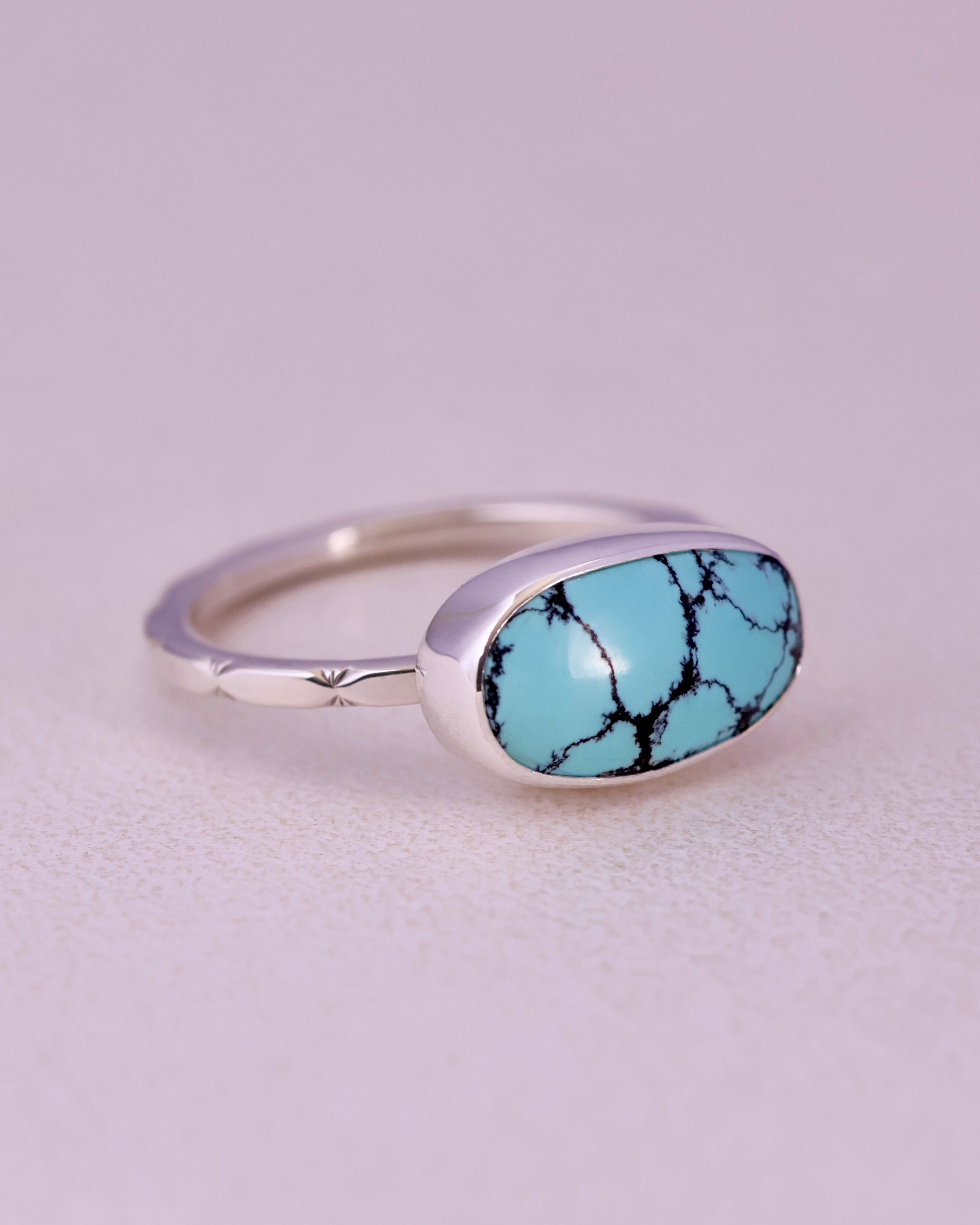 Blue turquoise stone ring with sterling silver faceted band on a light gray background