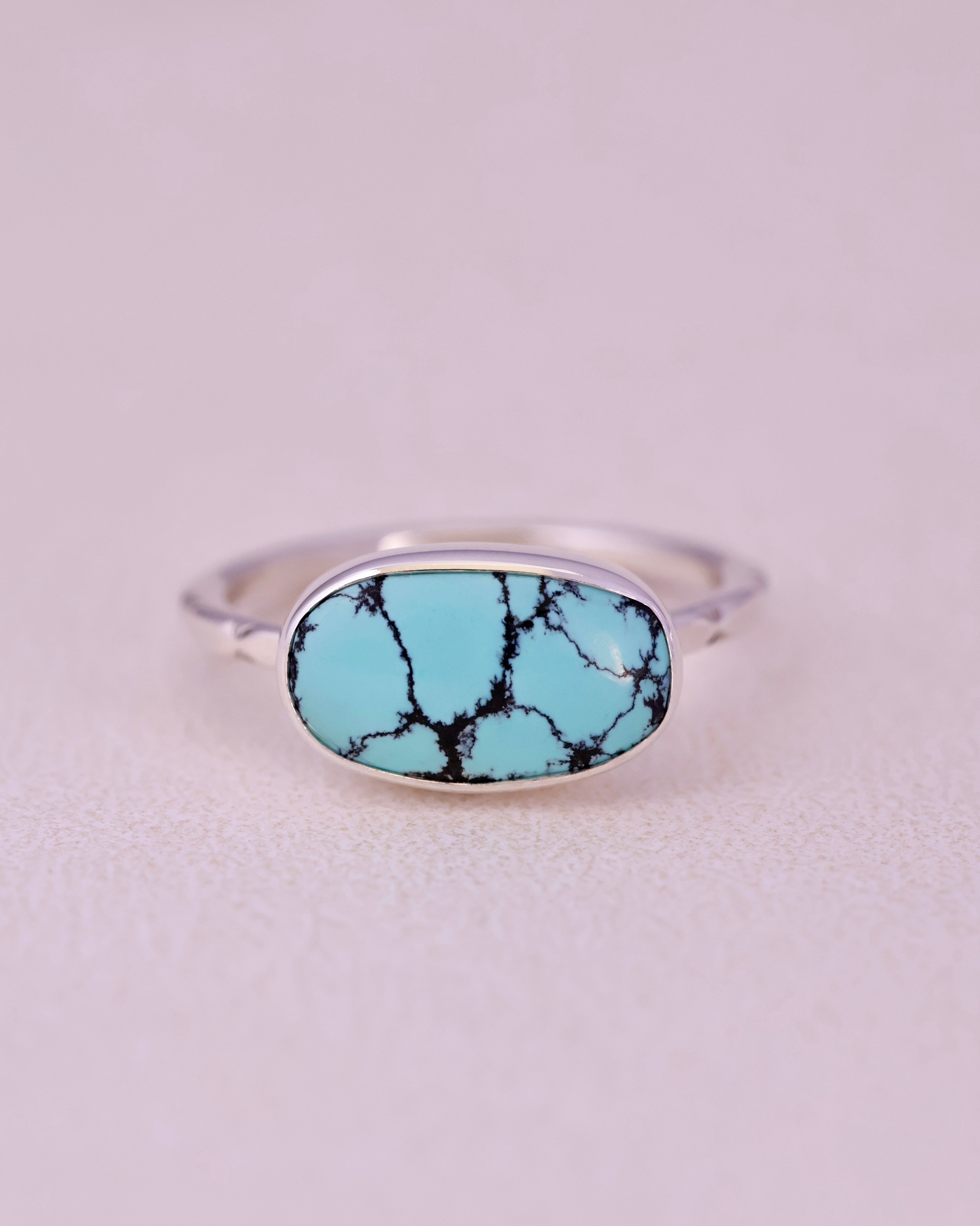 Blue turquoise stone ring with sterling silver faceted band on a light gray background
