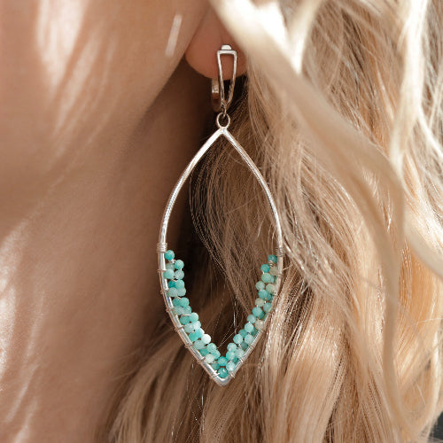 Close-up of a person with blonde hair wearing a handcrafted silver marquise-shaped earring decorated with small amazonite gemstone beads.