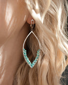 Close-up of a person with blonde hair wearing a handcrafted silver marquise-shaped earring decorated with small amazonite gemstone beads.