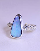 The Boulder Opal Ring by Lilac Sky Studio showcases a large, triangular blue opal in a bezel setting on a textured sterling silver band, exuding coastal charm.