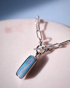 The Boulder Opal Necklace by Lilac Sky Studio features a sterling silver rectangular pendant with a marbled pattern in blue, pink, and green tones, shown on a smooth, light surface.