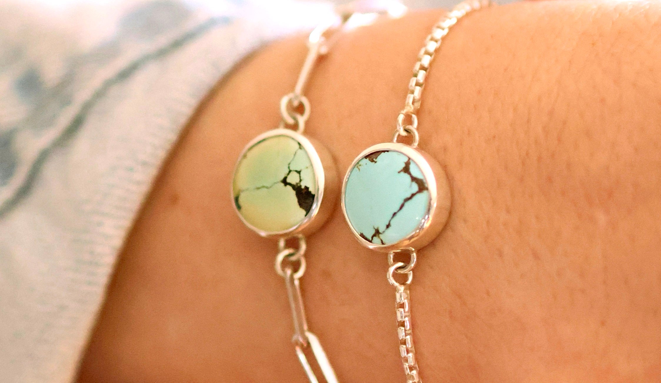 Close-up of a wrist wearing two handcrafted silver chain bracelets with round turquoise stone settings featuring natural veining, showcasing unique jewelry made from ethically sourced materials.