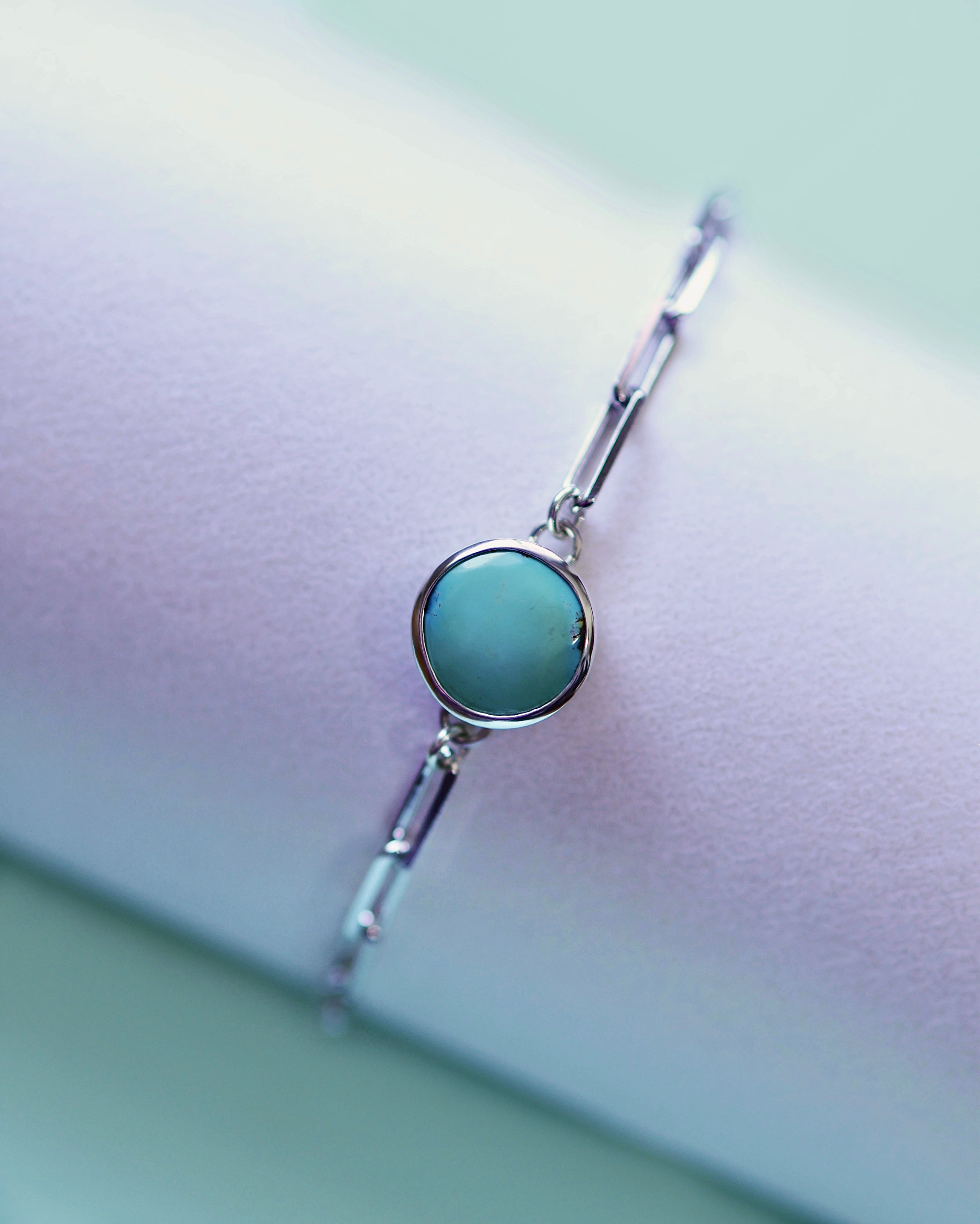 The Treasure Mountain Turquoise Bracelet No. 1 by Lilac Sky Studio features a round turquoise centerpiece on an adjustable sterling silver cable chain, beautifully displayed on a light-colored surface.
