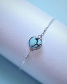 The Cloud Mountain Turquoise Bracelet No. 2 by Lilac Sky Studio features a round turquoise stone with dark veining, set in sterling silver with an adjustable box chain, shown on a pastel background.