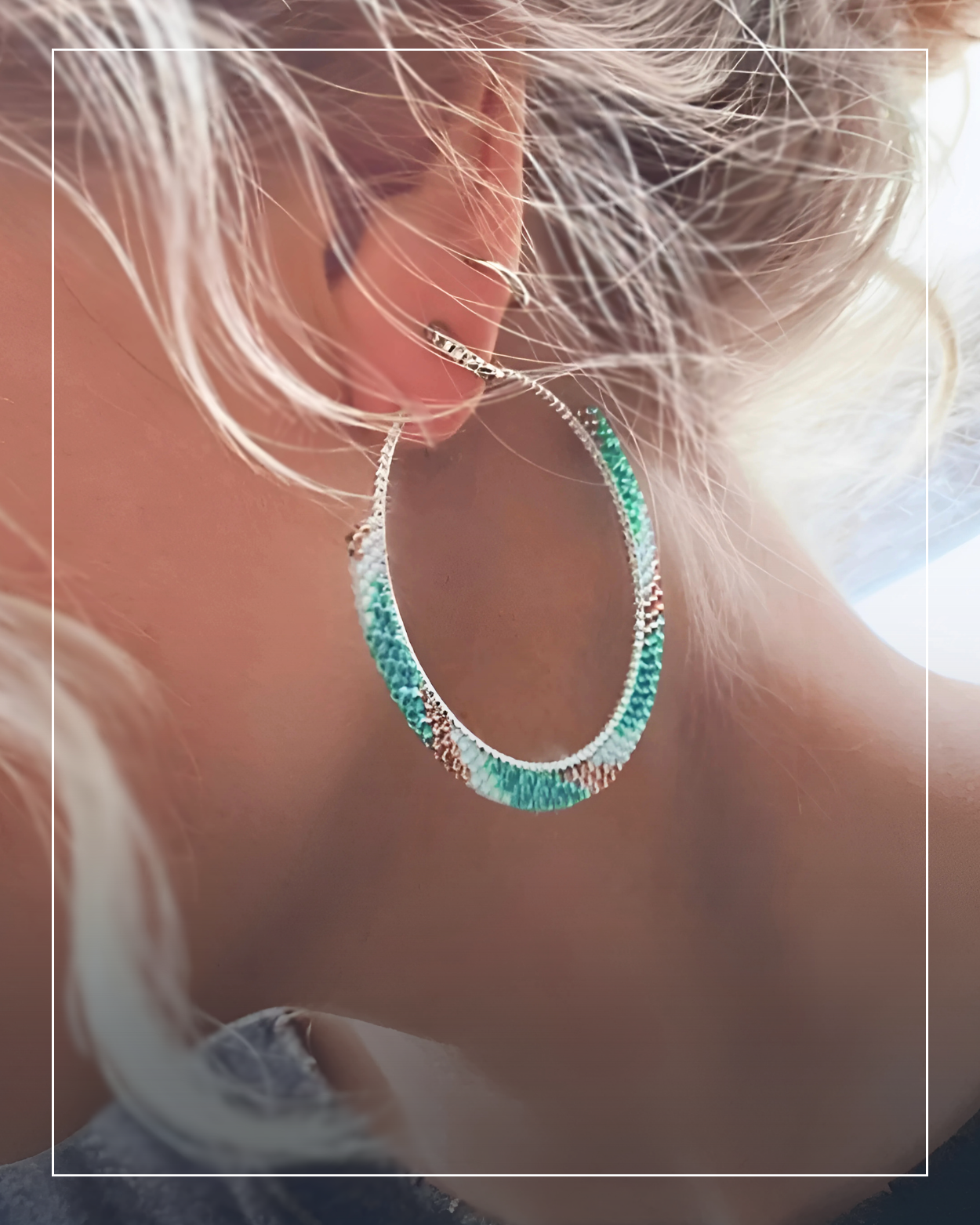 Close-up of a person's ear wearing a large, oval-shaped hoop earring with green and metallic jewelry accents, crafted from ethically sourced materials, against a softly blurred background.