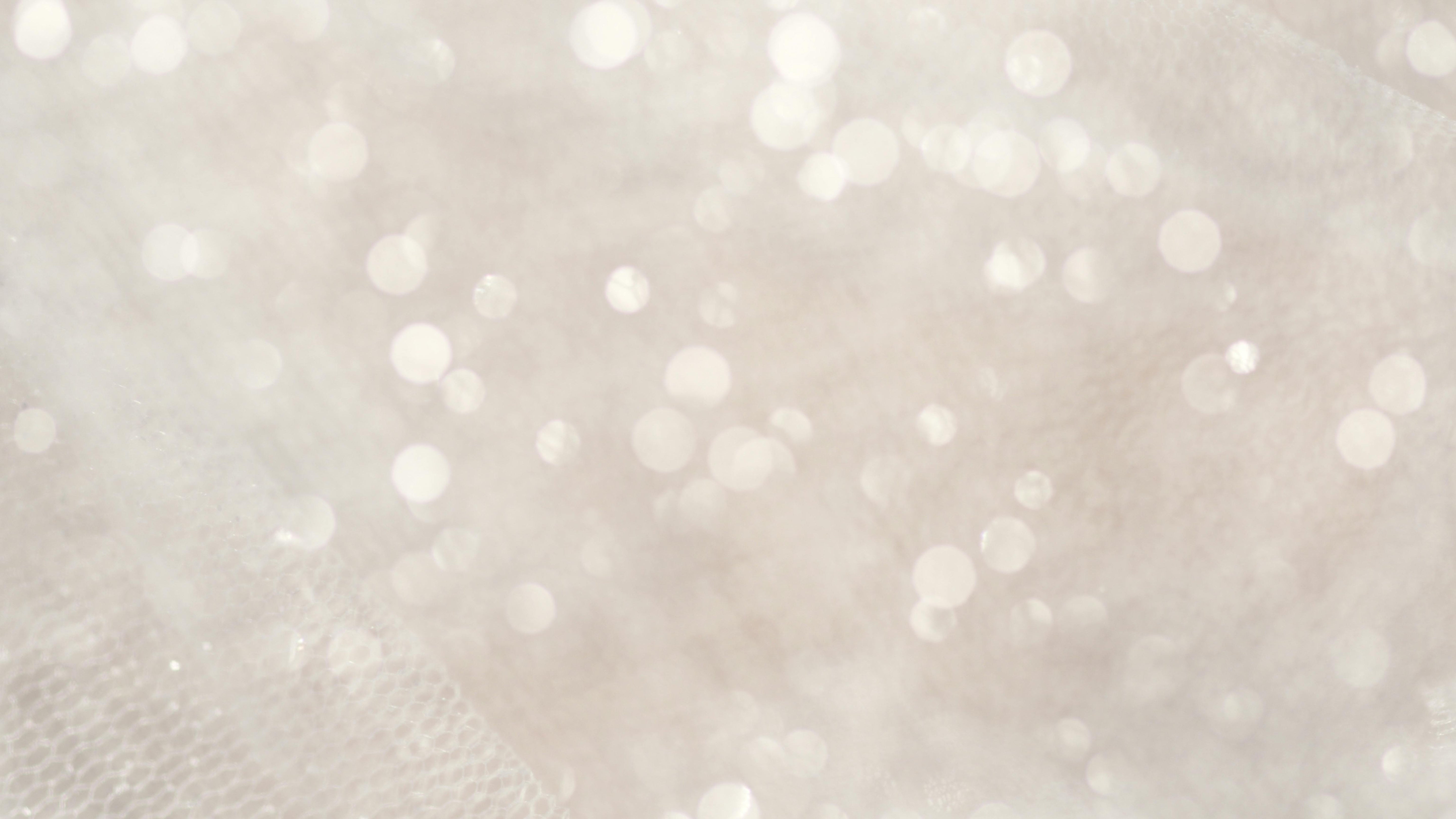 Close-up of a white, textured fabric with a soft, bokeh effect created by small, out-of-focus light spots, reminiscent of the shimmer found in ethically sourced gemstones.