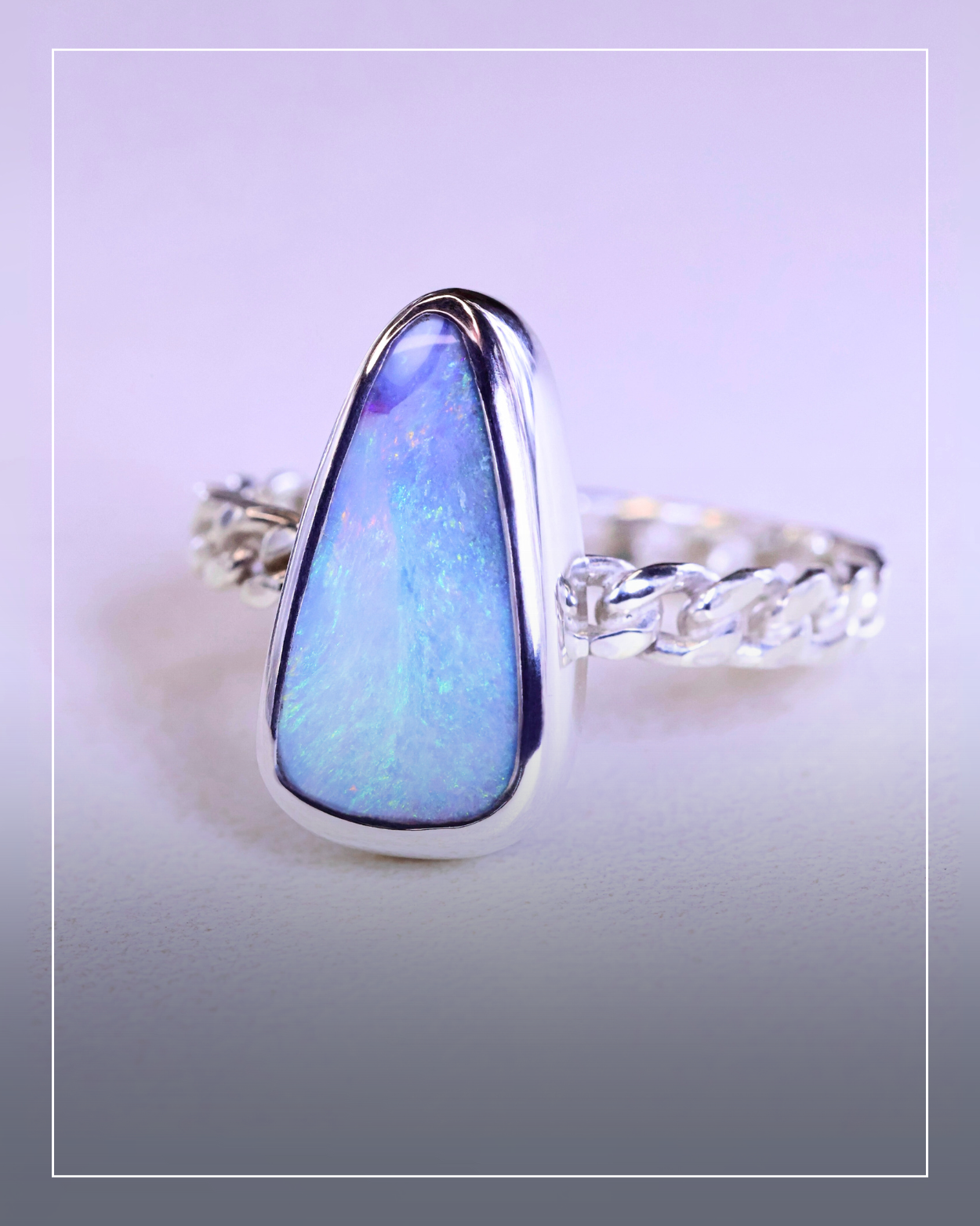 A silver ring with a large, triangular blue opal gemstone set in the center, featuring a handcrafted braided band design, displayed on a light surface.