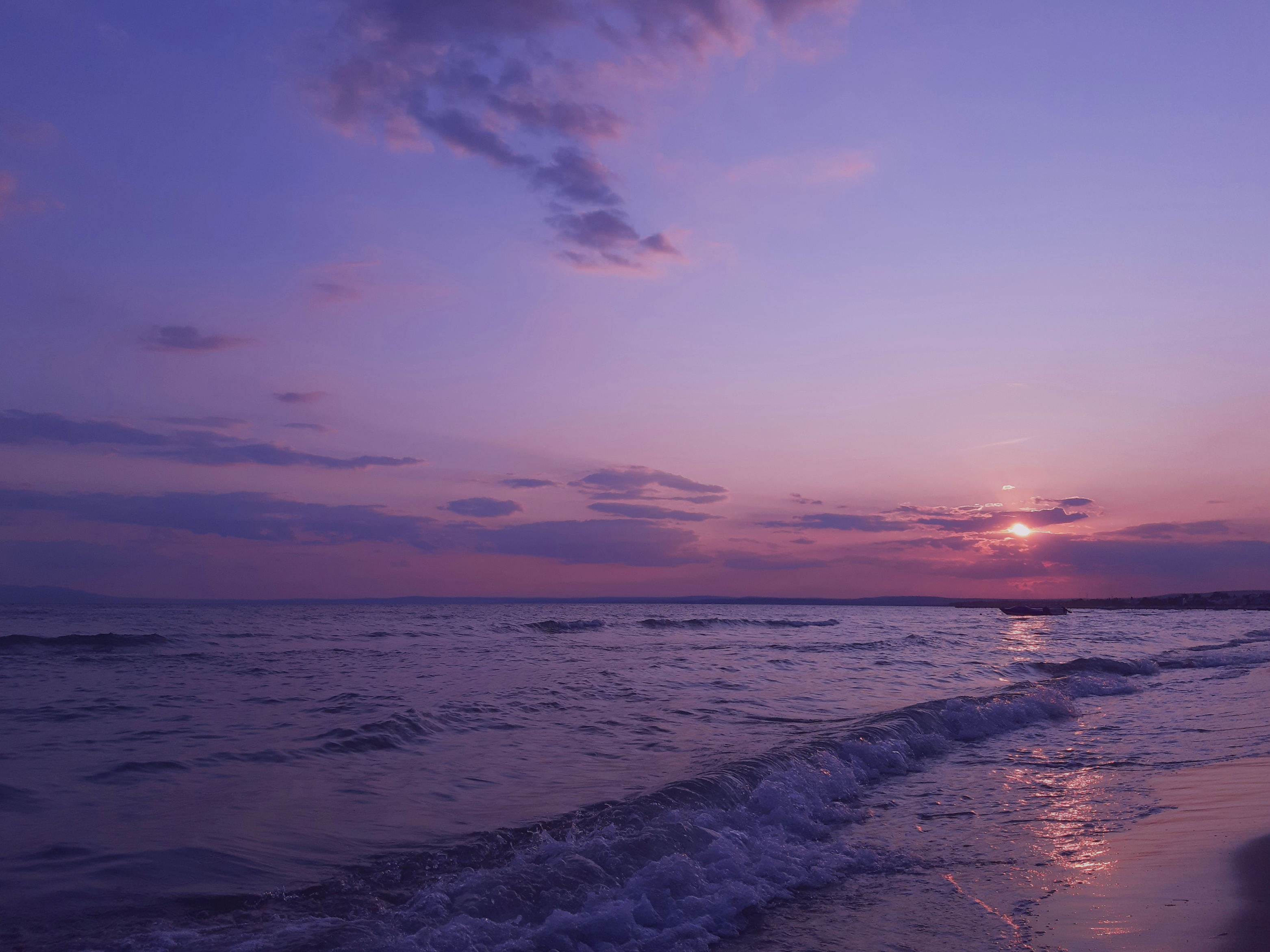 Waves gently roll onto a beach at sunset, with a purple and pink sky and scattered clouds over the horizon—nature’s beauty as exquisite as handcrafted jewelry.