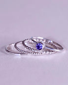 The Tanzanite Ring Stacker Set by Lilac Sky Studio features four sterling silver rings—one with a round Tanzanite gemstone and three with unique band designs—perfect for anyone who loves distinctive gemstone jewelry.