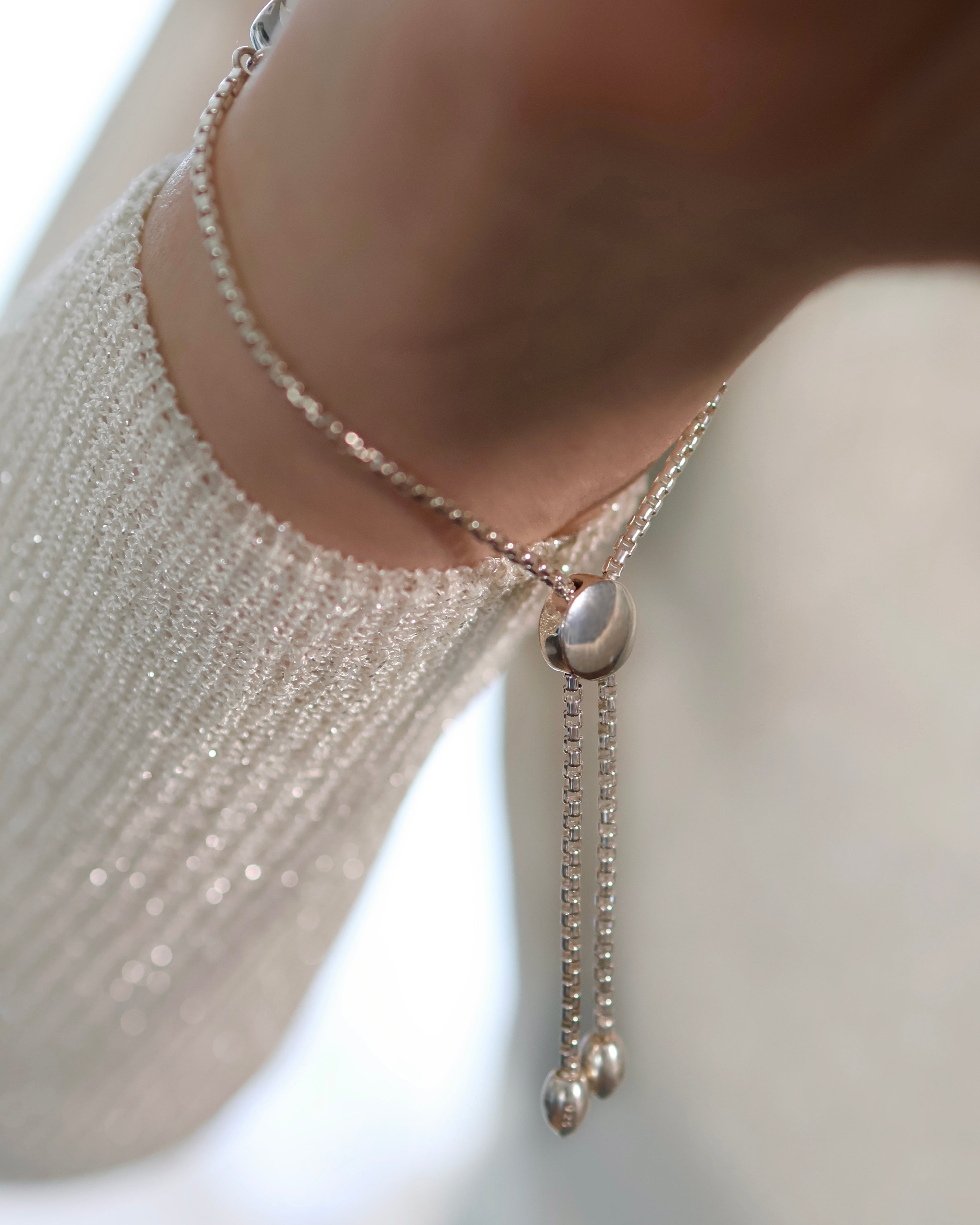 A close-up of a wrist wearing Lilac Sky Studio's Cloud Mountain Turquoise Bracelet No. 2, featuring an adjustable box chain and sliding clasp, over a sparkly, light-colored knit sleeve.