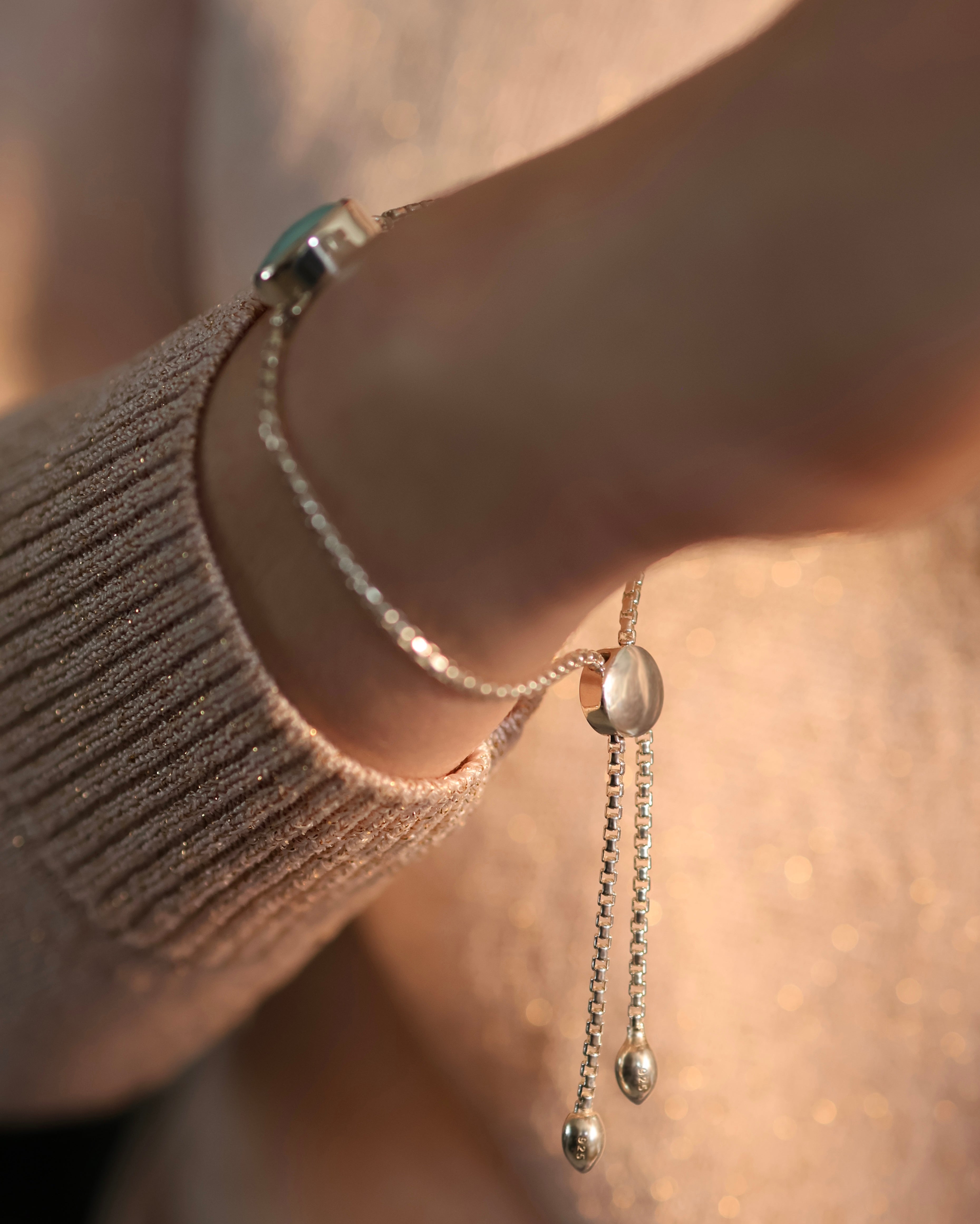 A close-up of a wrist wearing Lilac Sky Studio's Cloud Mountain Turquoise Bracelet No. 4, an adjustable .925 Sterling Silver box chain with two dangling ends, shown against a beige glittery sweater.