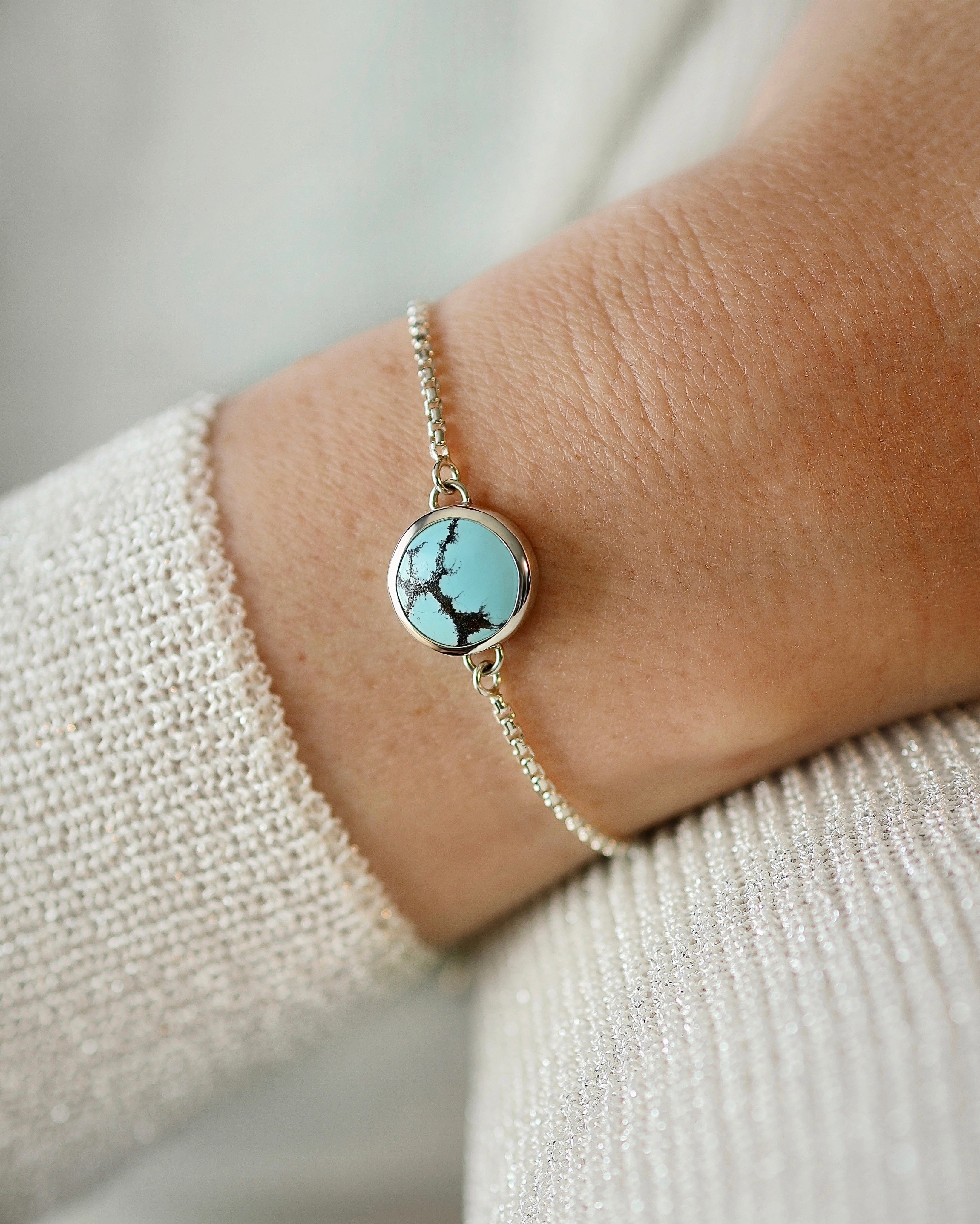 A close-up of the Lilac Sky Studio Cloud Mountain Turquoise Bracelet No. 2, featuring a round turquoise stone set in sterling silver, shown on a wrist against light, textured fabric.