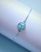 The Cloud Mountain Turquoise Bracelet No. 4 by Lilac Sky Studio features a .925 sterling silver adjustable box chain and a round turquoise stone with dark veins, beautifully displayed on a light surface.