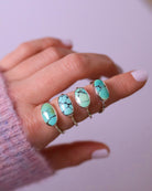 Hand wearing four turquoise sterling silver rings on a light background