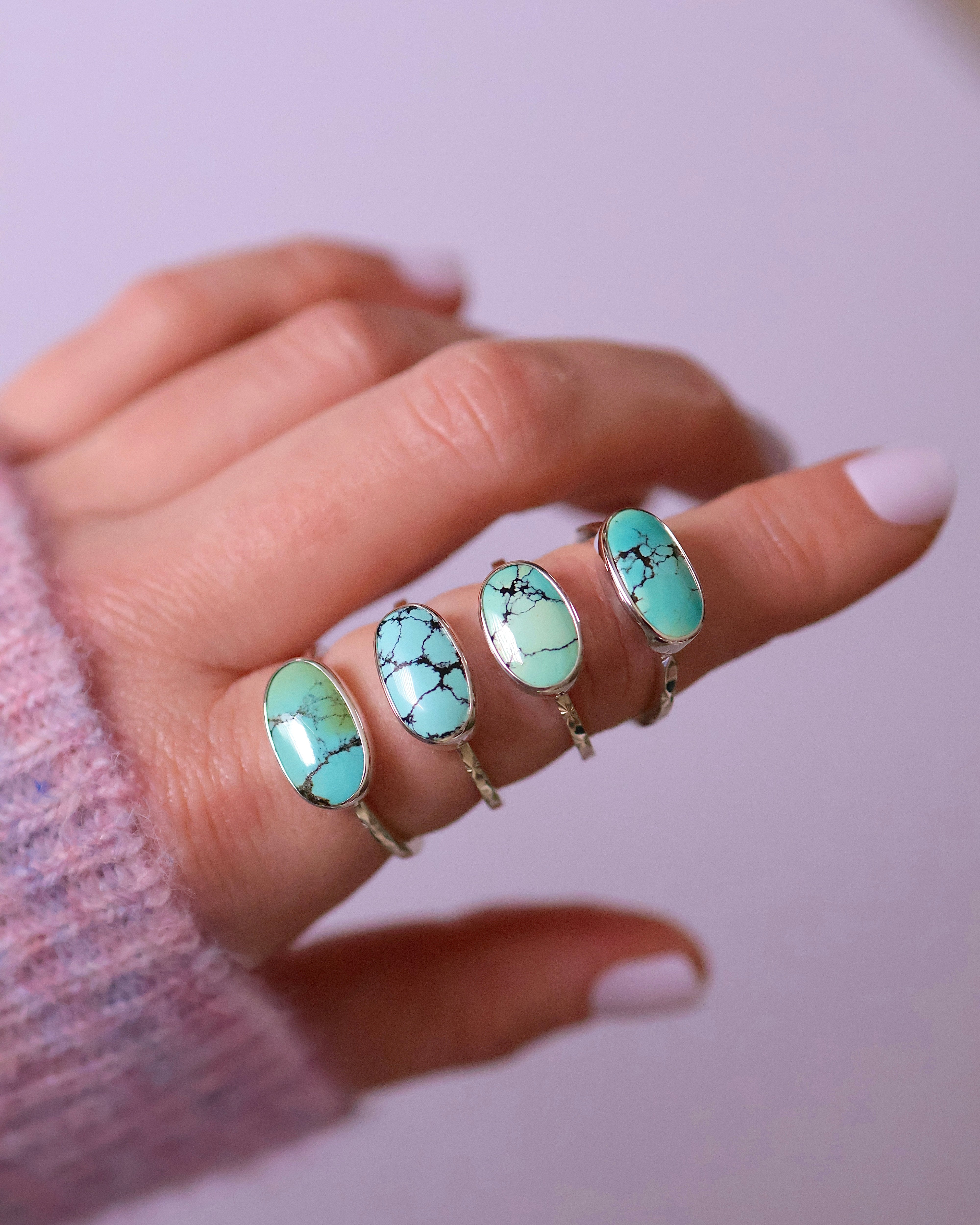 Hand wearing four turquoise sterling silver rings on a light background