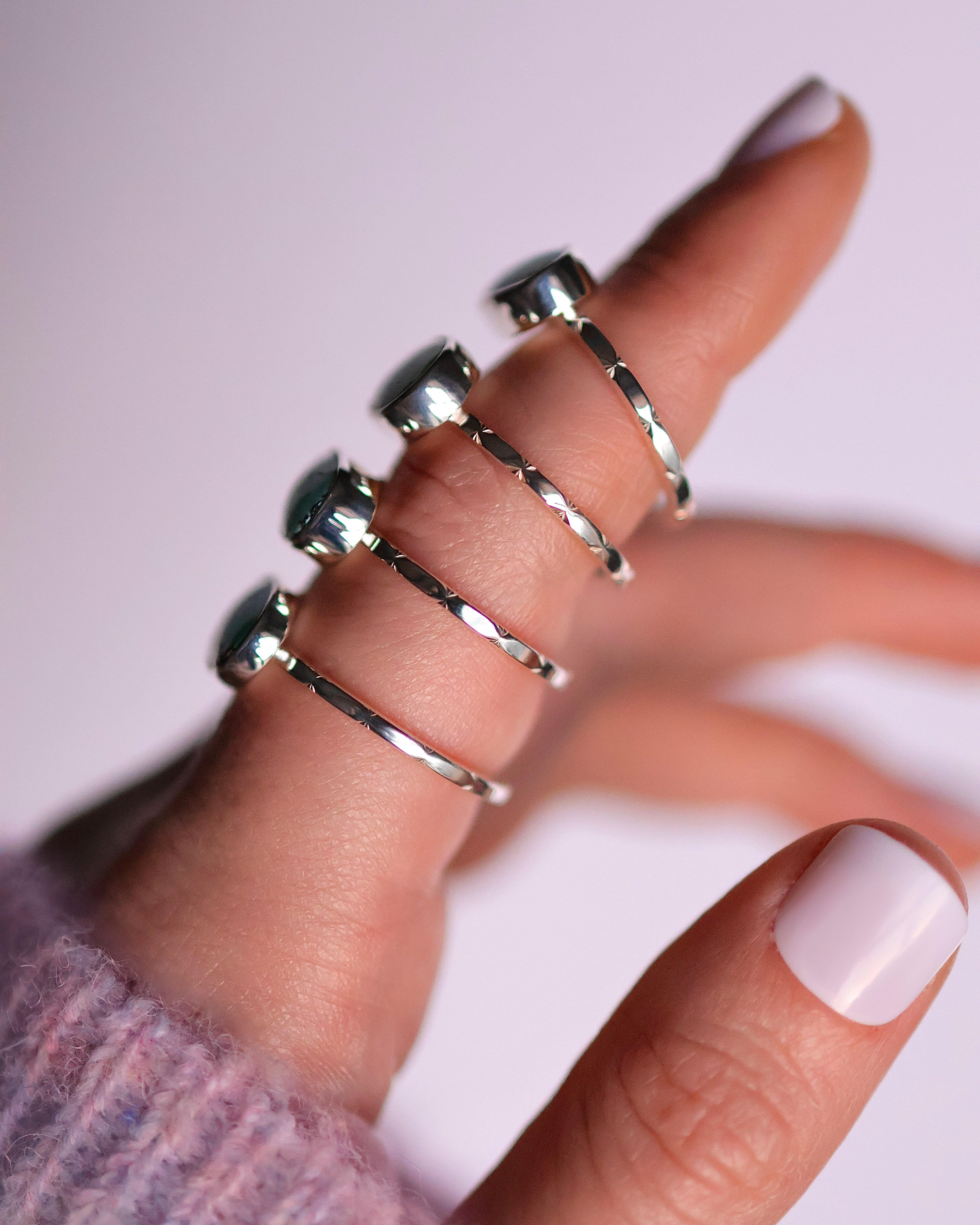 Close-up of a hand wearing four sterling silver turquoise rings, showcasing the faceted bands on a light background