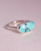 Turquoise stone ring with sterling silver faceted band on a light gray background