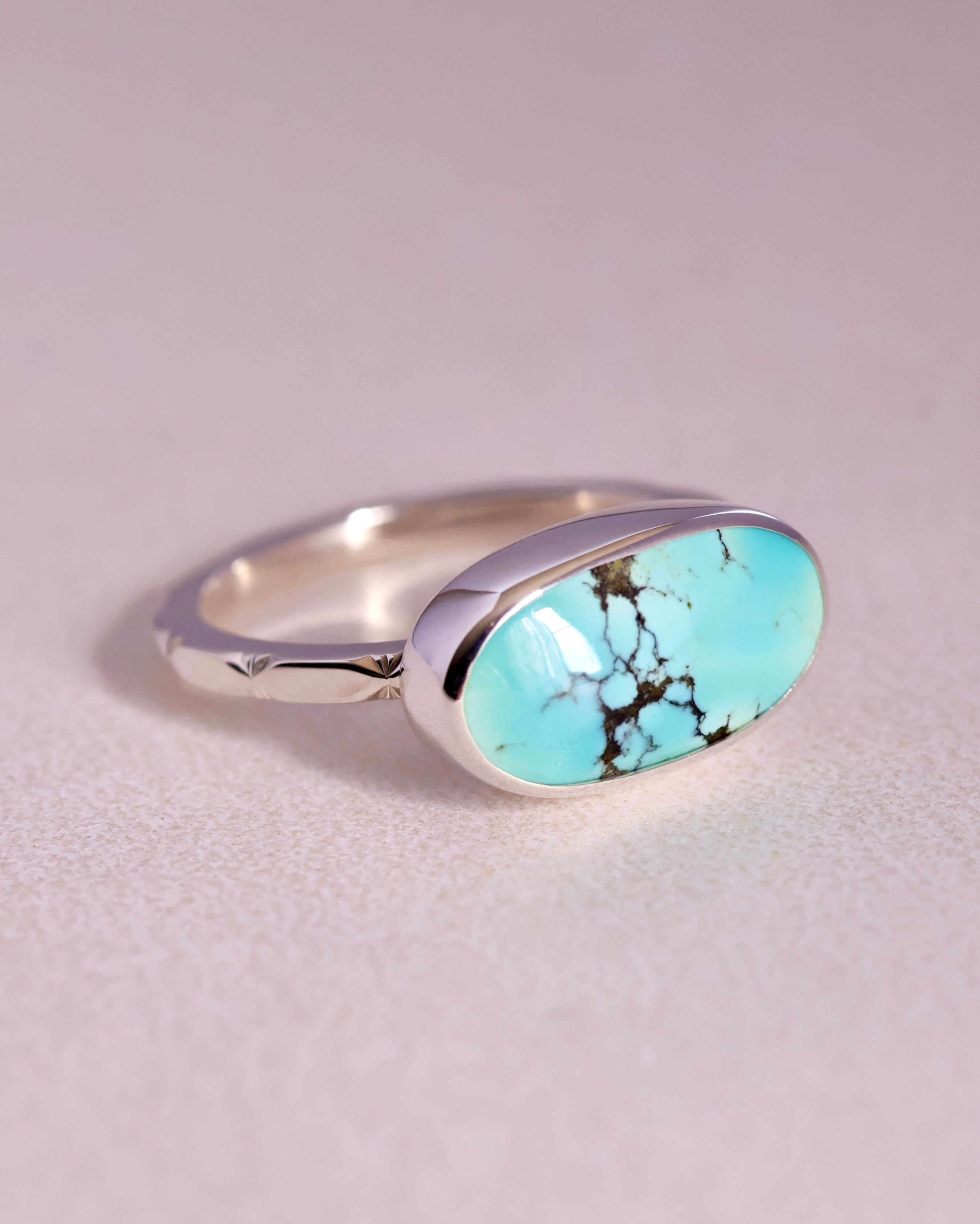 Turquoise stone ring with sterling silver faceted band on a light gray background