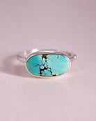 Turquoise stone ring with sterling silver faceted band on a light gray background
