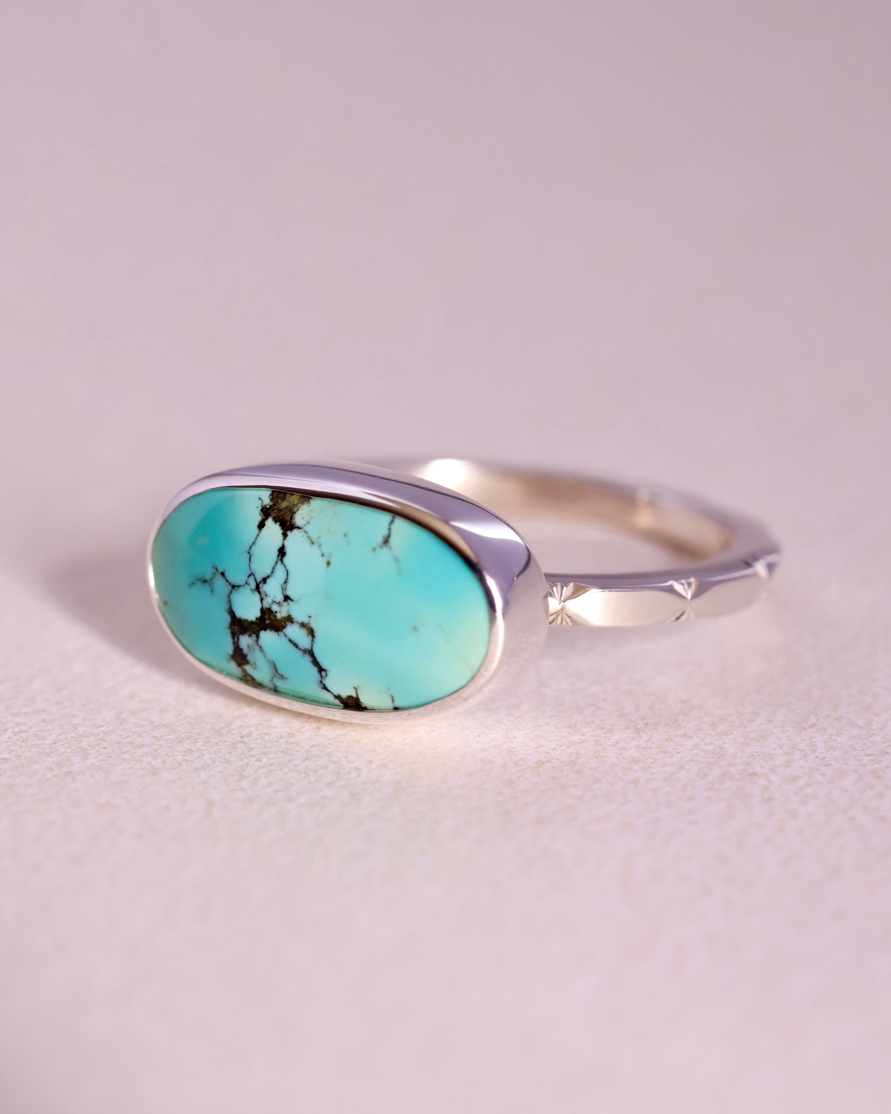 Turquoise stone ring with sterling silver faceted band on a light gray background