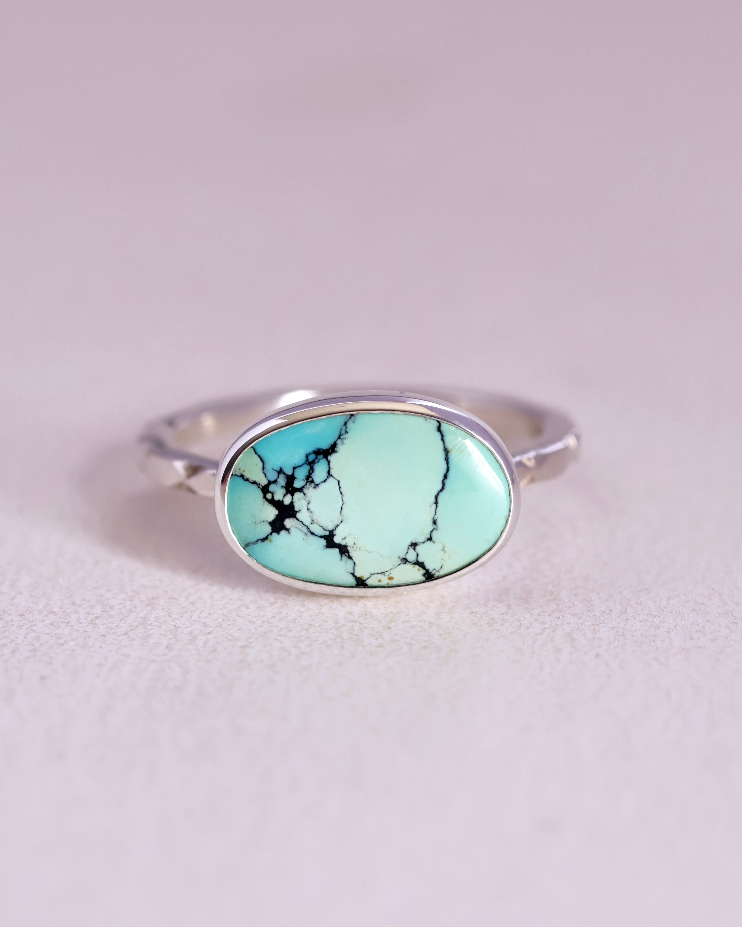 Sterling Silver ring with a turquoise stone and a starburst pattern band on a light gray background