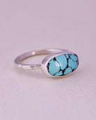 Blue turquoise stone ring with sterling silver faceted band on a light gray background