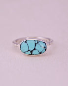 Blue turquoise stone ring with sterling silver faceted band on a light gray background