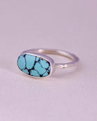 Blue turquoise stone ring with sterling silver faceted band on a light gray background